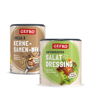 Zwei GEFRO Dosen: Omega-3 Kerne-Samen-Mix und Gartenkräuter Salat Dressing, freigestellt auf schwarzem Hintergrund
