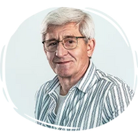 Porträt eines älteren Mannes mit Brille und weiß-grauem Haar in gestreiftem Hemd vor hellem Hintergrund