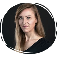 Porträt einer Frau mit langen hellbraunen Haaren, schwarzen Oberteil und neutralem Blick vor dunklem Hintergrund