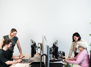 Drei Personen arbeiten gemeinsam im Büro an Computern und Laptop, Besprechung am Schreibtisch im Team