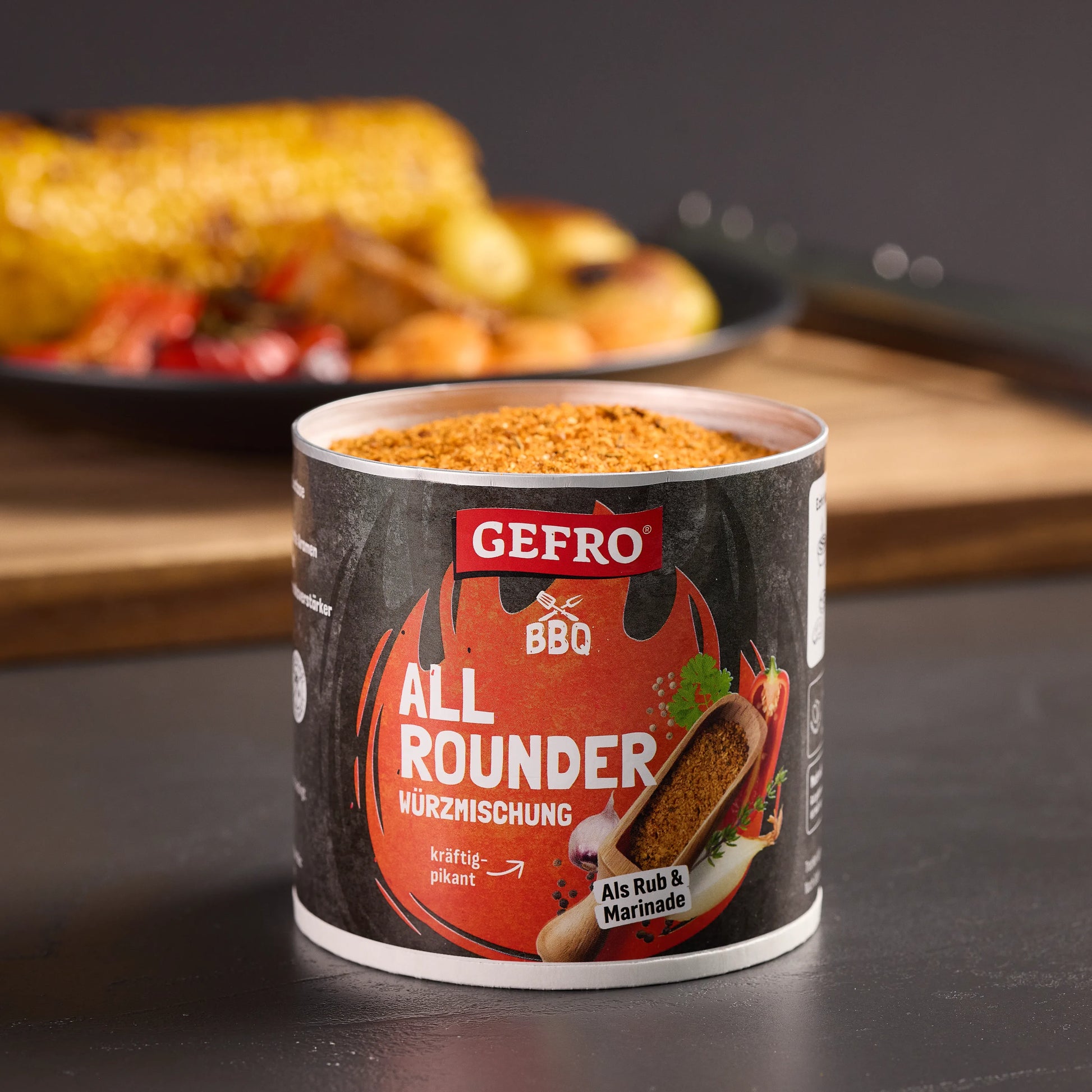 Dose mit GEFRO BBQ Allrounder Würzmischung, geöffnet auf Tisch, dahinter gegrillter Mais und Gemüse unscharf.