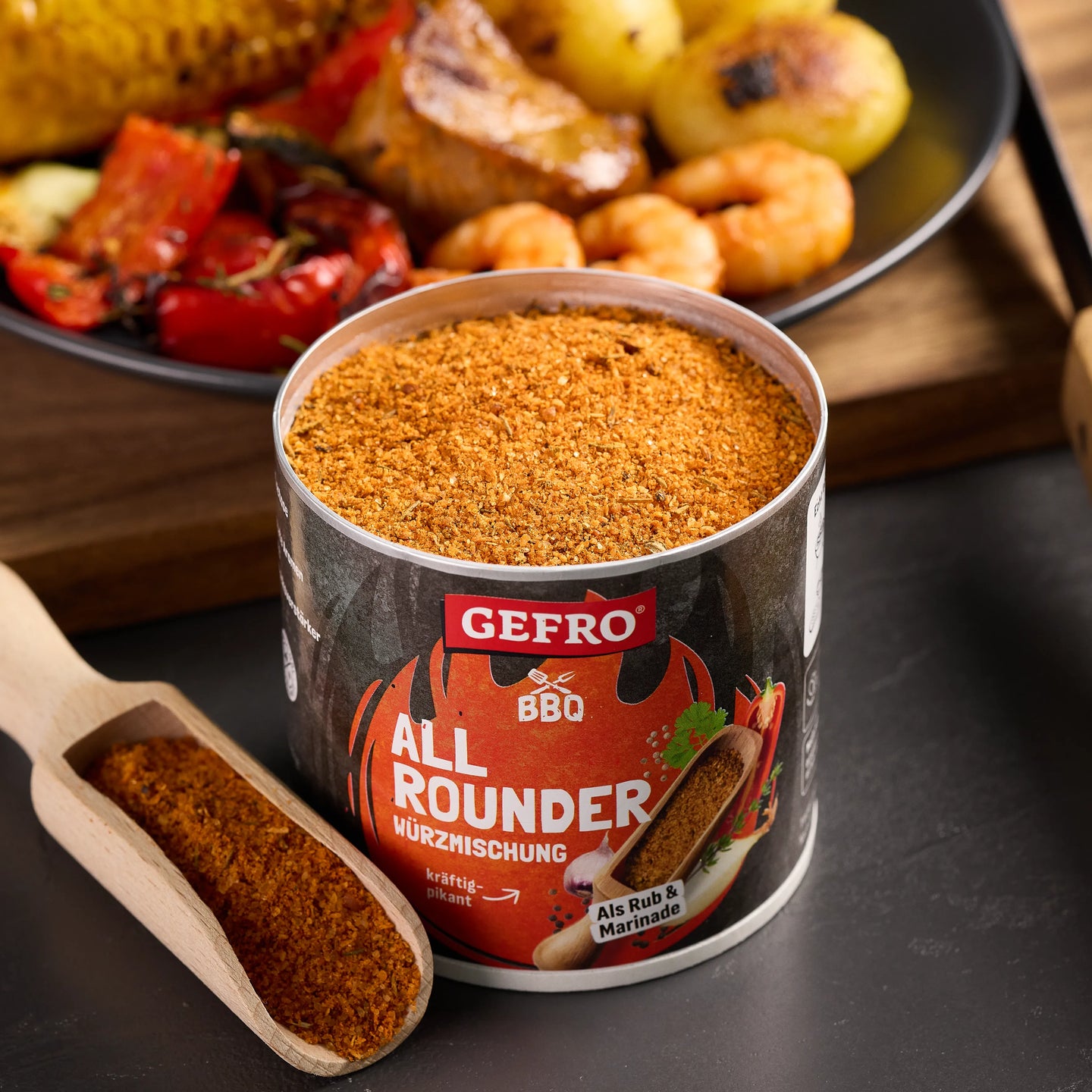Offene Dose GEFRO BBQ Allrounder Würzmischung mit Holzschaufel, davor gegrilltes Gemüse, Kartoffeln und Garnelen.