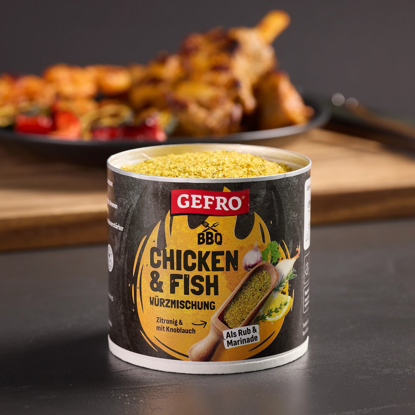 Offene Dose GEFRO BBQ Chicken & Fish Würzmischung auf dunkler Fläche, im Hintergrund gegrilltes Hähnchen unscharf