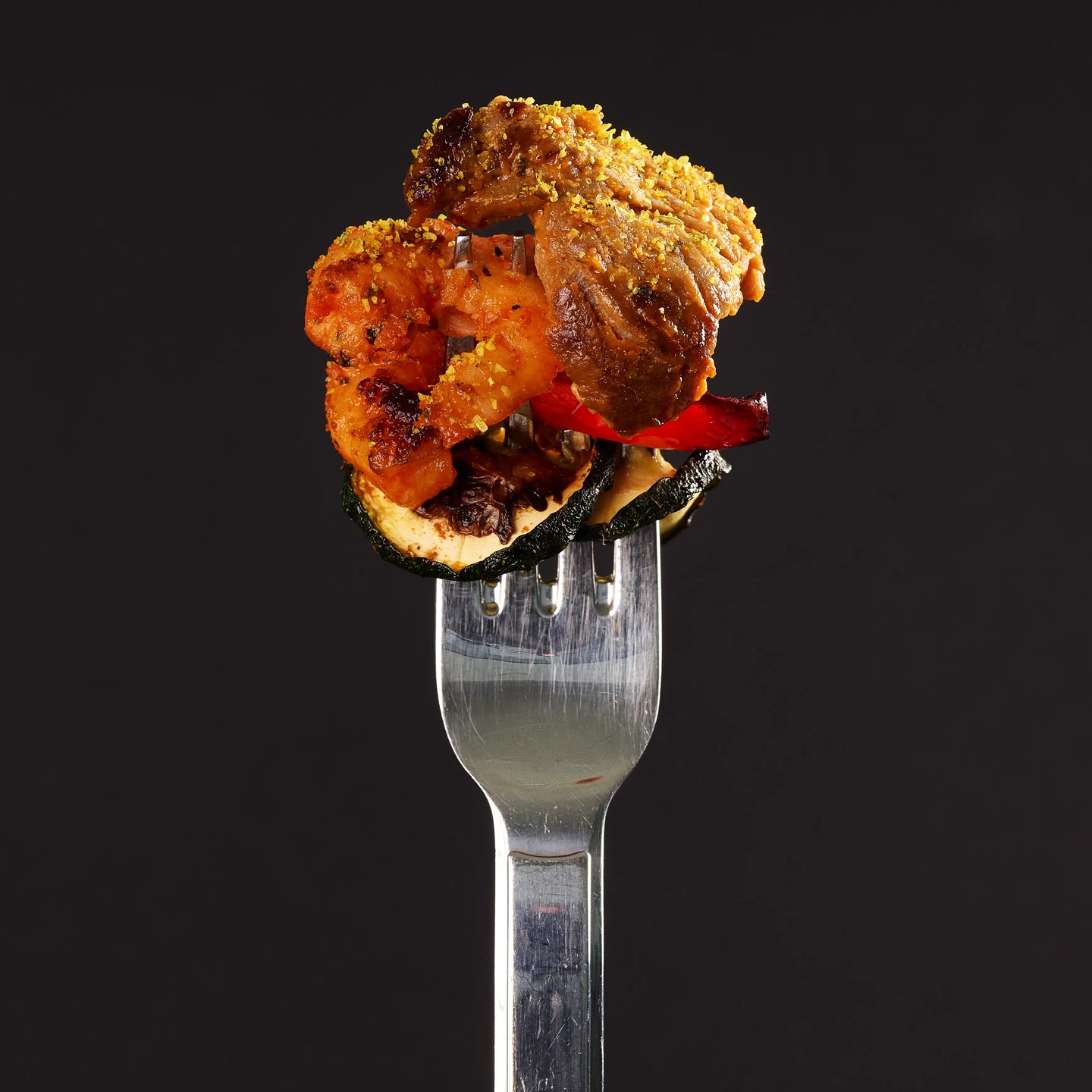Gabel mit gegrilltem Fleisch, Garnelen und Gemüse vor schwarzem Hintergrund, appetitlich als Serviervorschlag präsentiert
