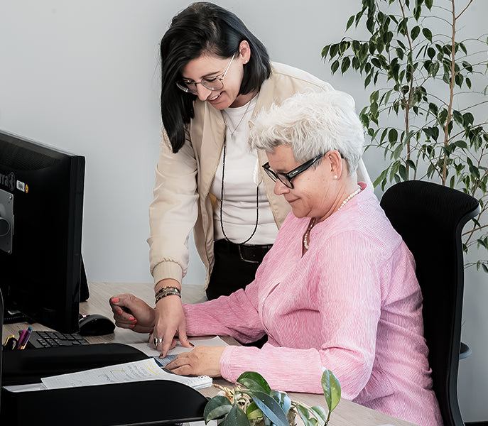 Zwei Frauen am Schreibtisch prüfen gemeinsam Unterlagen und arbeiten konzentriert am Computer im Büro.