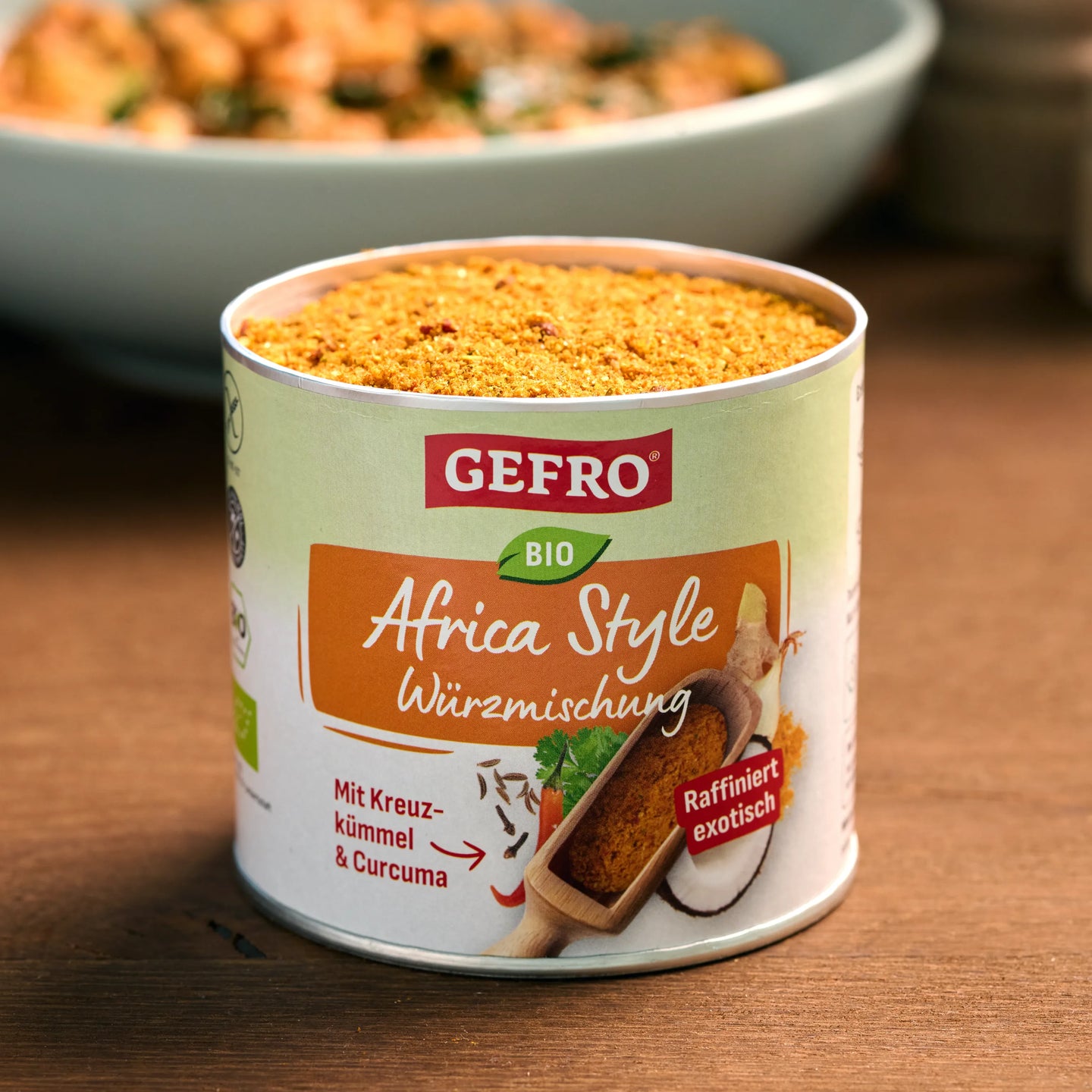 Dose mit GEFRO Bio Africa Style Würzmischung, geöffnet auf Holztisch, im Hintergrund eine Schüssel mit Gericht.