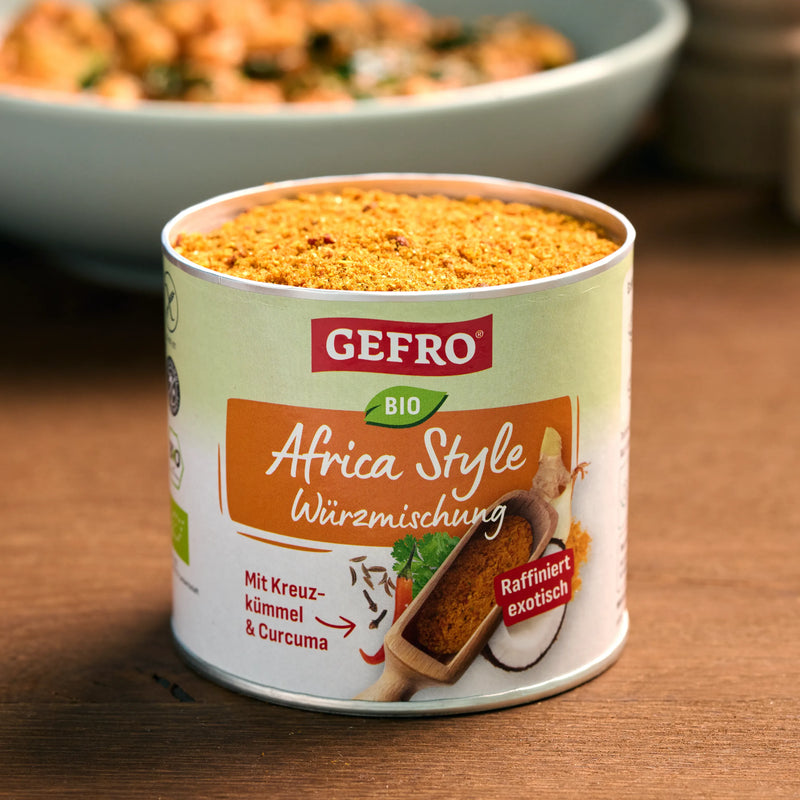Dose mit GEFRO Bio Africa Style Würzmischung, geöffnet auf Holztisch, im Hintergrund eine Schüssel mit Gericht.