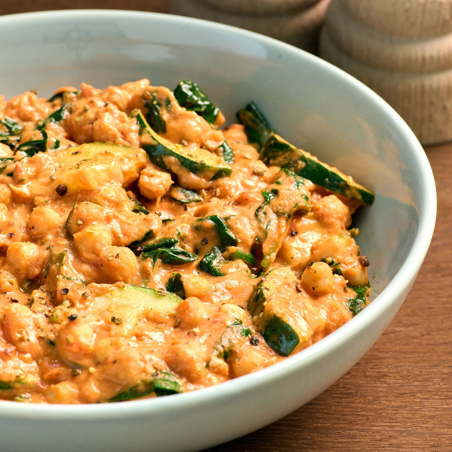 Schüssel mit cremigem Kichererbsen-Eintopf mit Zucchini und Spinat auf Holztisch, servierfertig angerichtet
