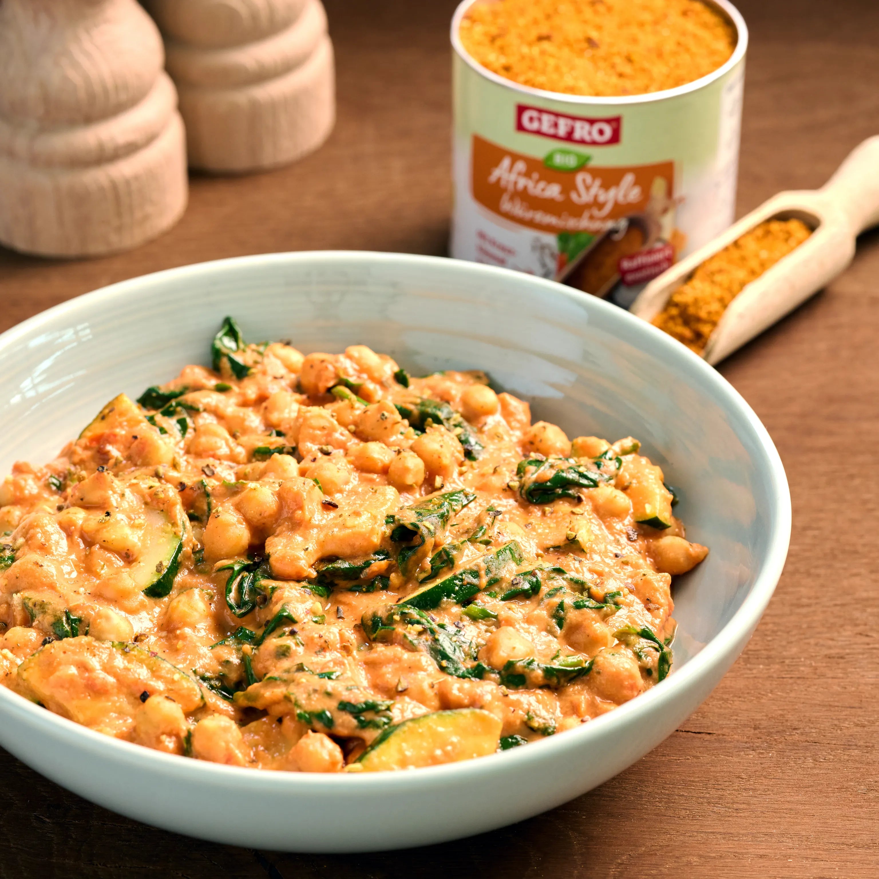 Schüssel mit cremigem Kichererbsen-Gemüse-Curry, daneben Gewürzdose und Löffel mit orangener Würzmischung