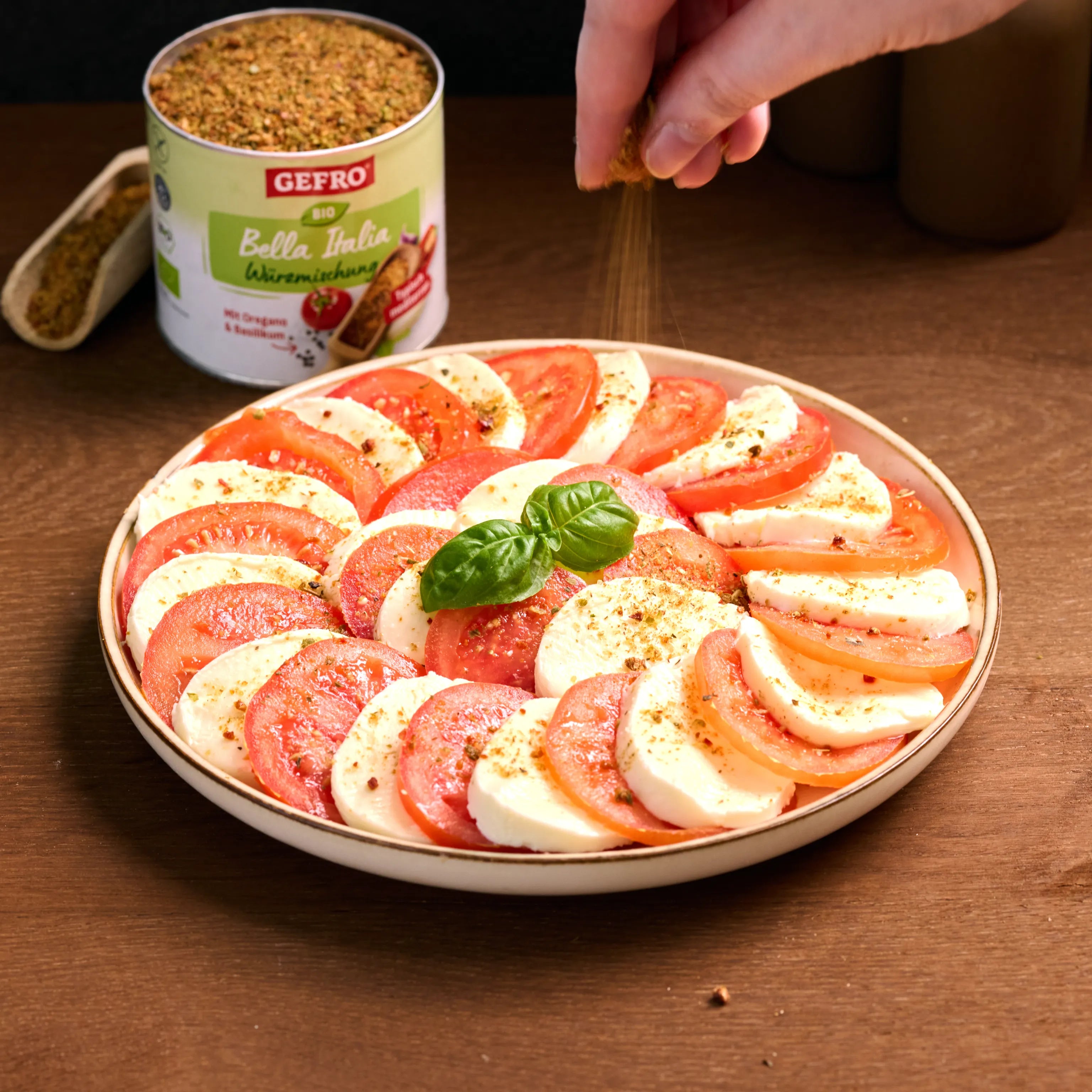 Caprese-Salat mit Tomaten und Mozzarella auf einem Teller, mit Basilikum und Gewürzmischung bestreut.