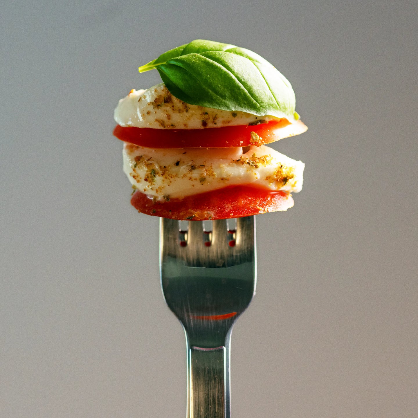 Gabel mit gestapelten Scheiben aus Mozzarella und Tomate, oben mit frischem Basilikum und Gewürzen garniert