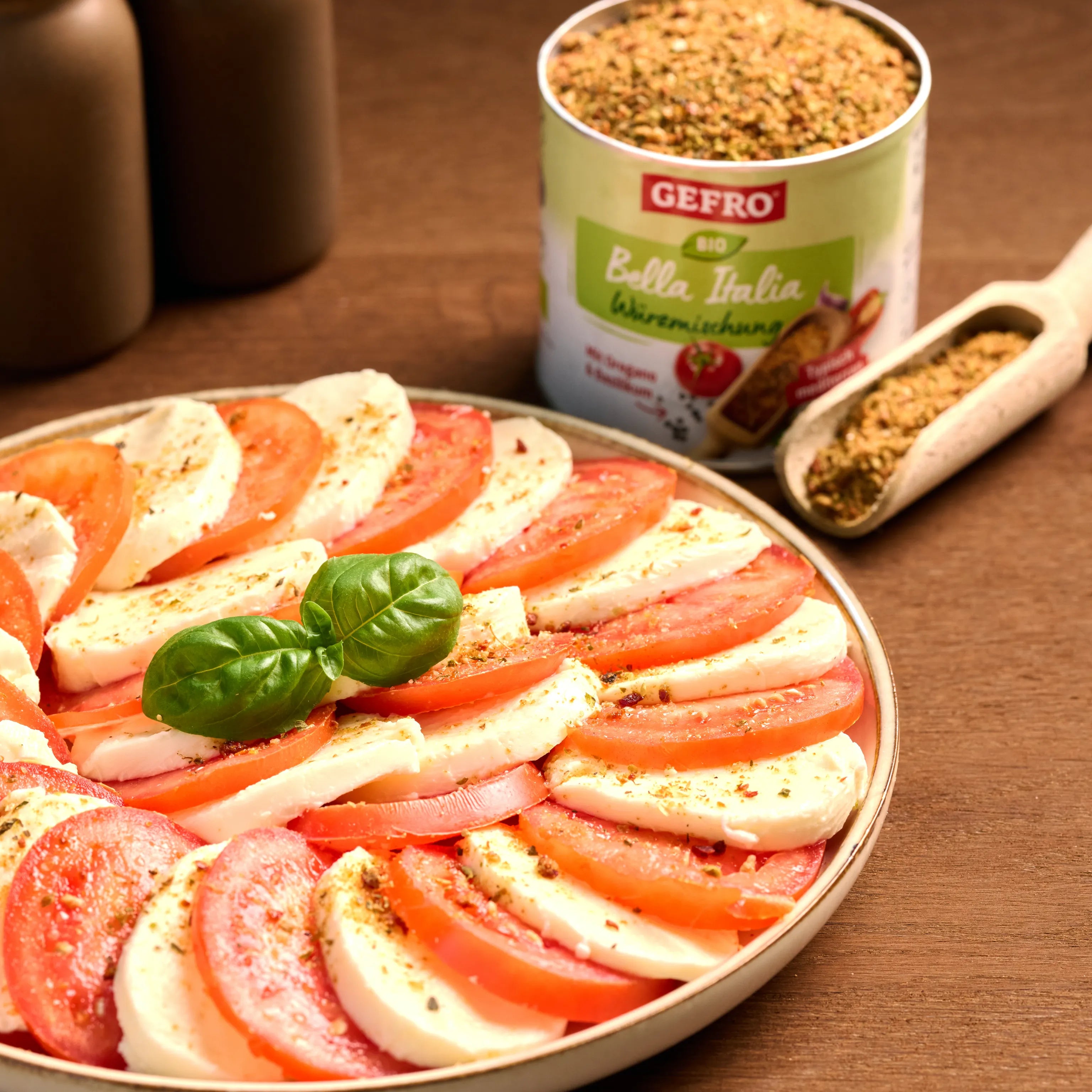 Caprese-Salat mit Tomaten, Mozzarella und Basilikum auf einem Teller, daneben italienische Gewürzmischung von Gefro