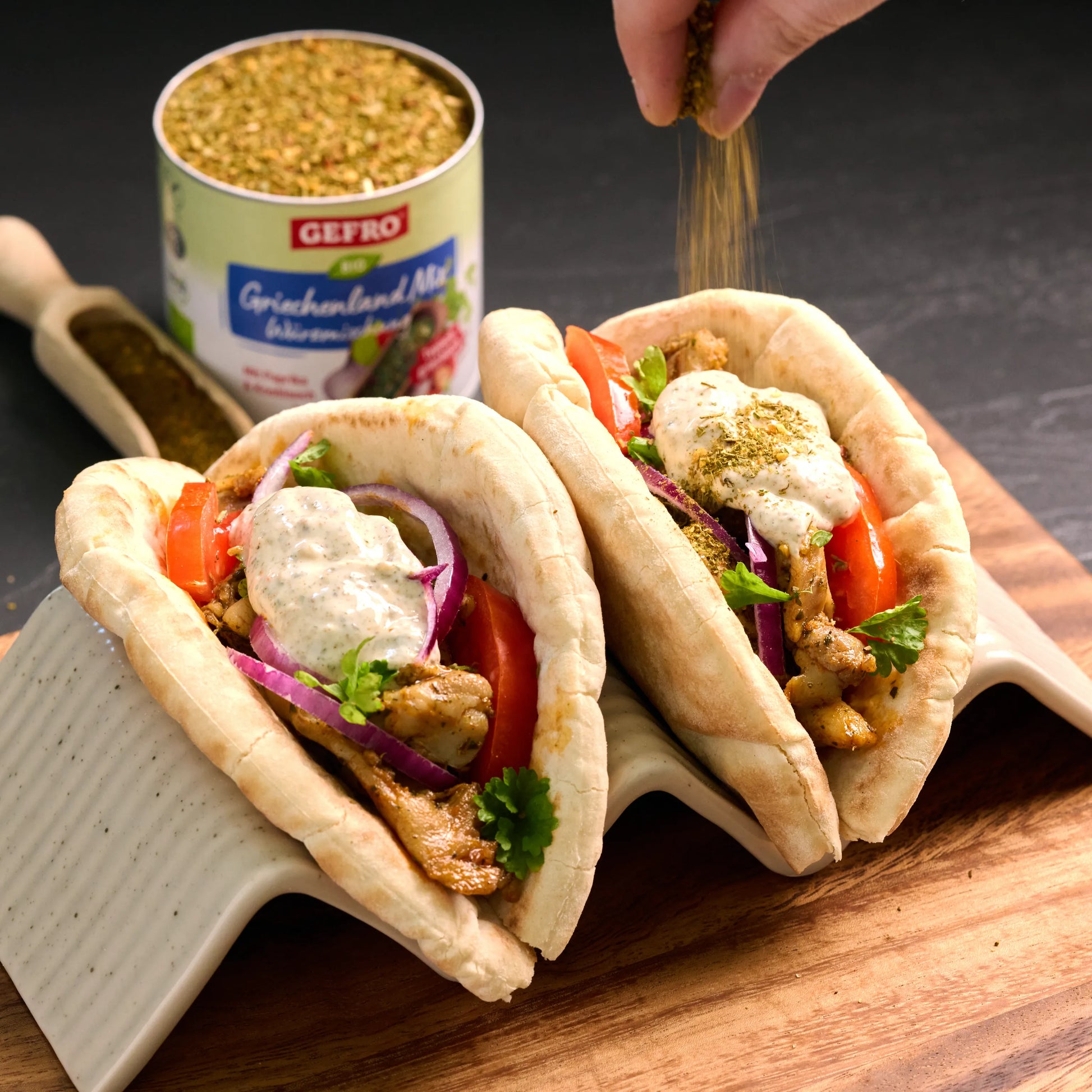 Zwei gefüllte Pita-Taschen mit Fleisch, Tomaten, roten Zwiebeln und cremiger Sauce, oben mit Gewürz bestreut