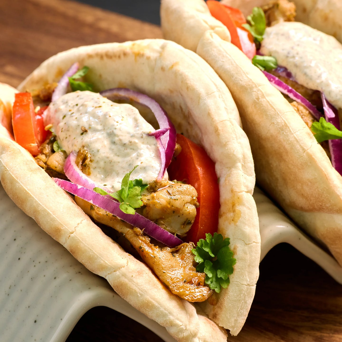 Gefüllte Pita mit Hähnchen, Tomaten, roten Zwiebeln, Kräutern und heller Sauce auf einem Servierständer