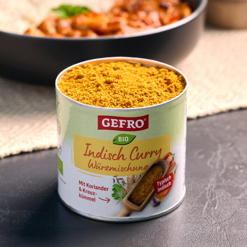 Offene Dose mit Bio indischer Curry-Würzmischung von GEFRO, gefüllt mit gelbem Gewürzpulver auf dunkler Fläche
