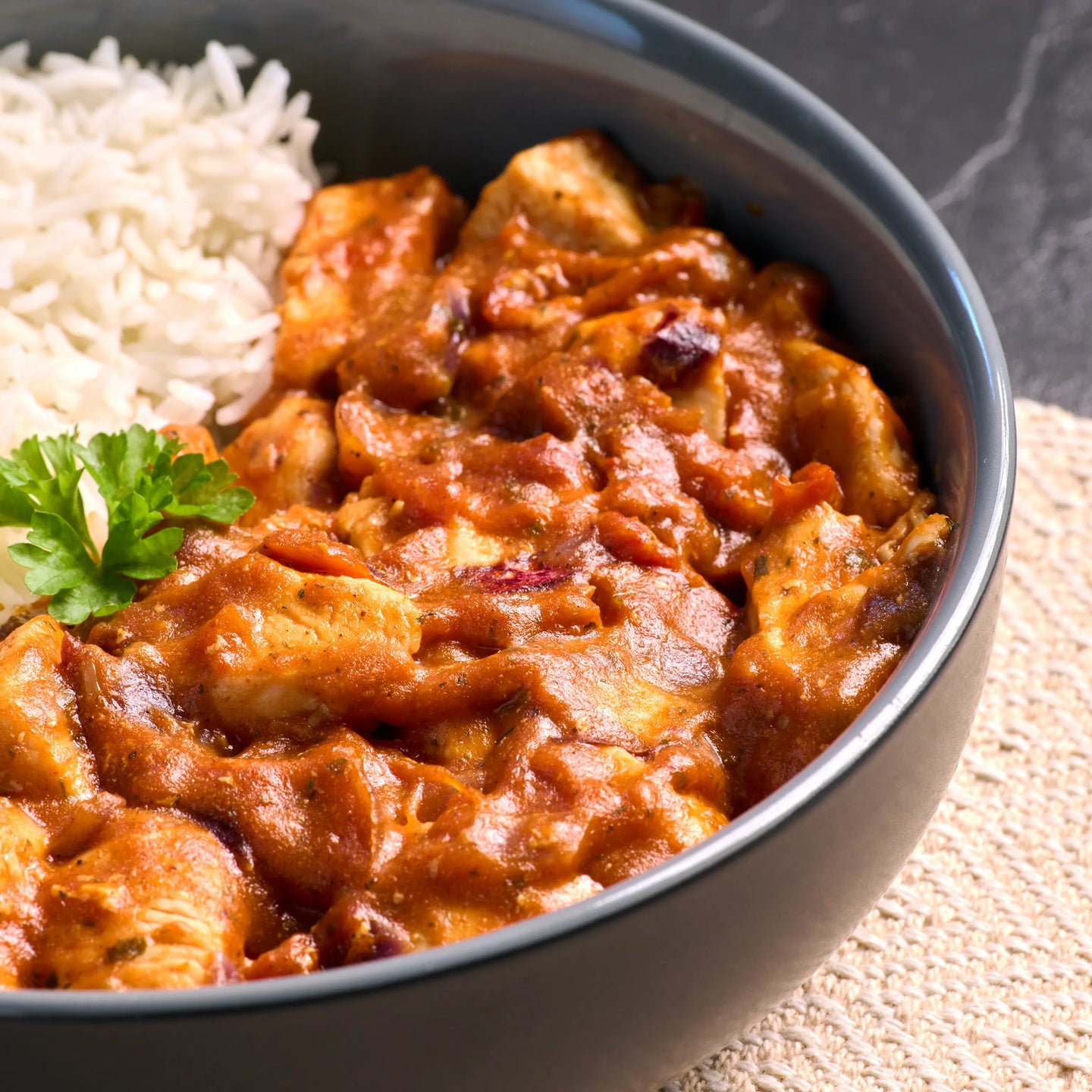 Schwarze Schale mit cremigem Hähnchen-Curry in roter Soße, dazu weißer Reis und etwas Petersilie als Beilage