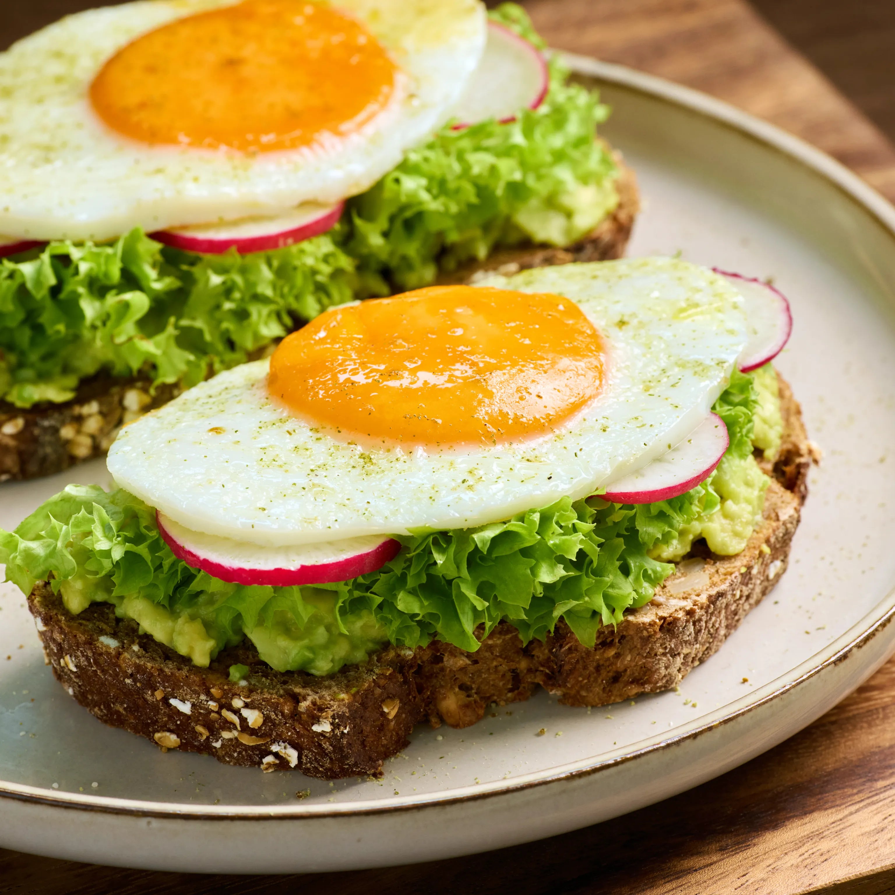 Zwei belegte Brote mit Avocado, Salat, Radieschen und Spiegelei auf einem Teller, serviert als frischer Snack