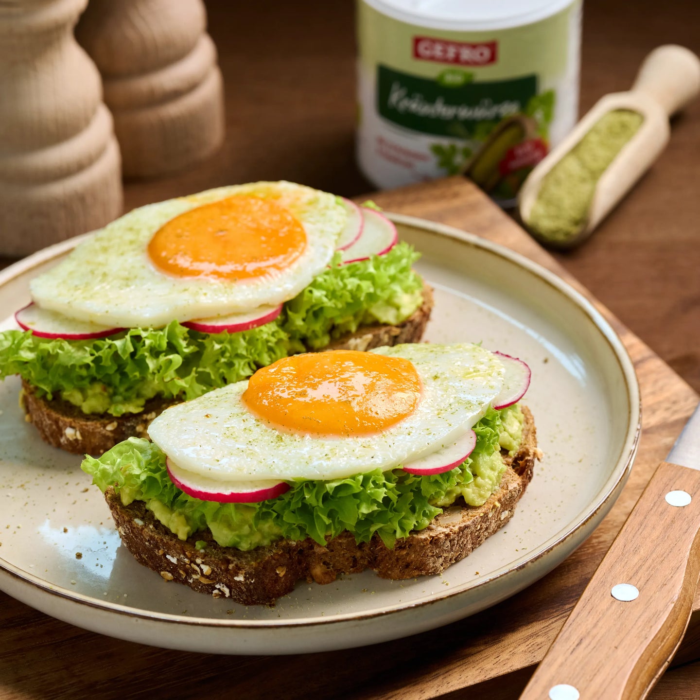 Zwei belegte Brote mit Salat, Radieschen und Spiegelei auf einem Teller, angerichtet auf einem Holzbrett.