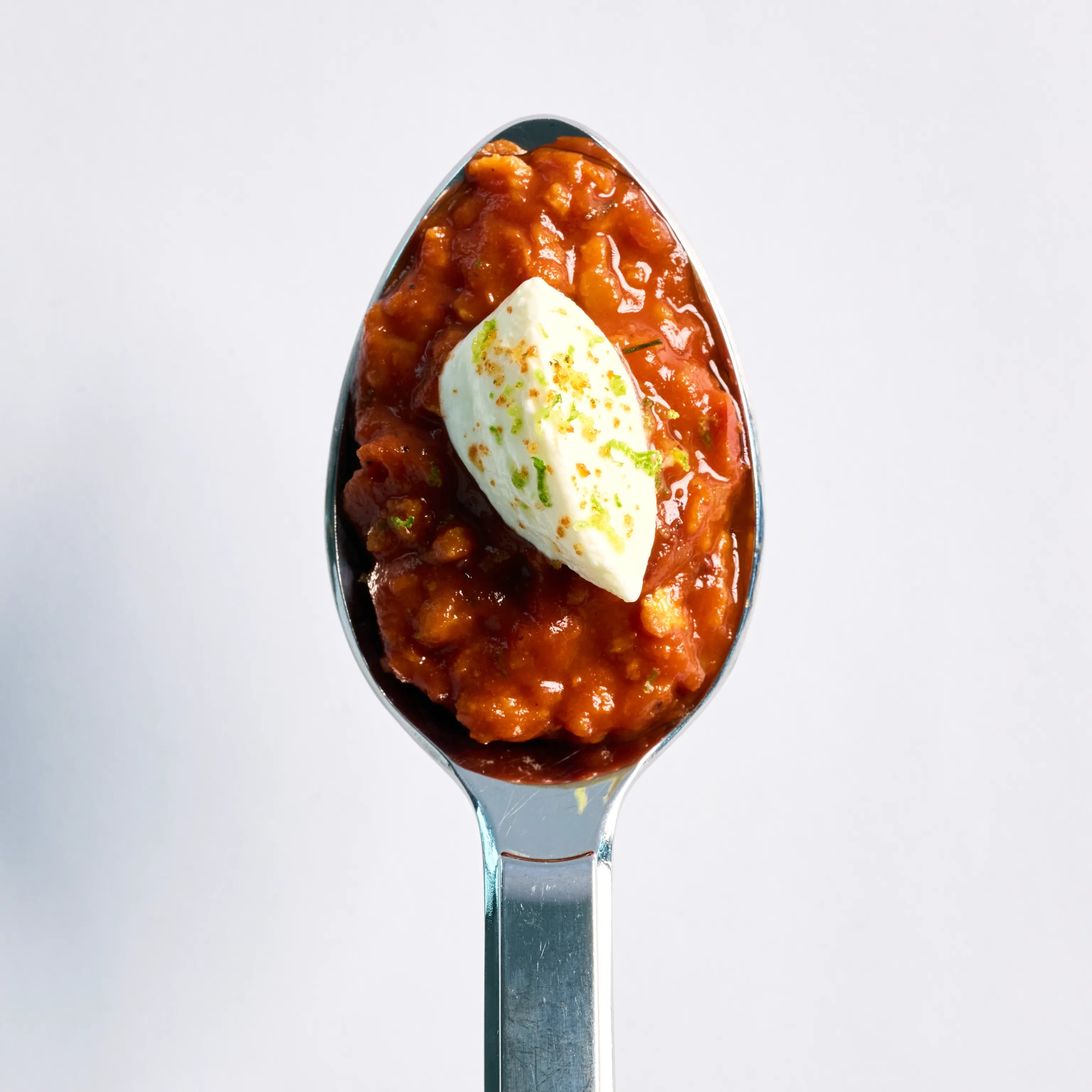 Löffel mit rotem Tomatenragout und einem Klecks heller Creme, von oben fotografiert vor hellem Hintergrund