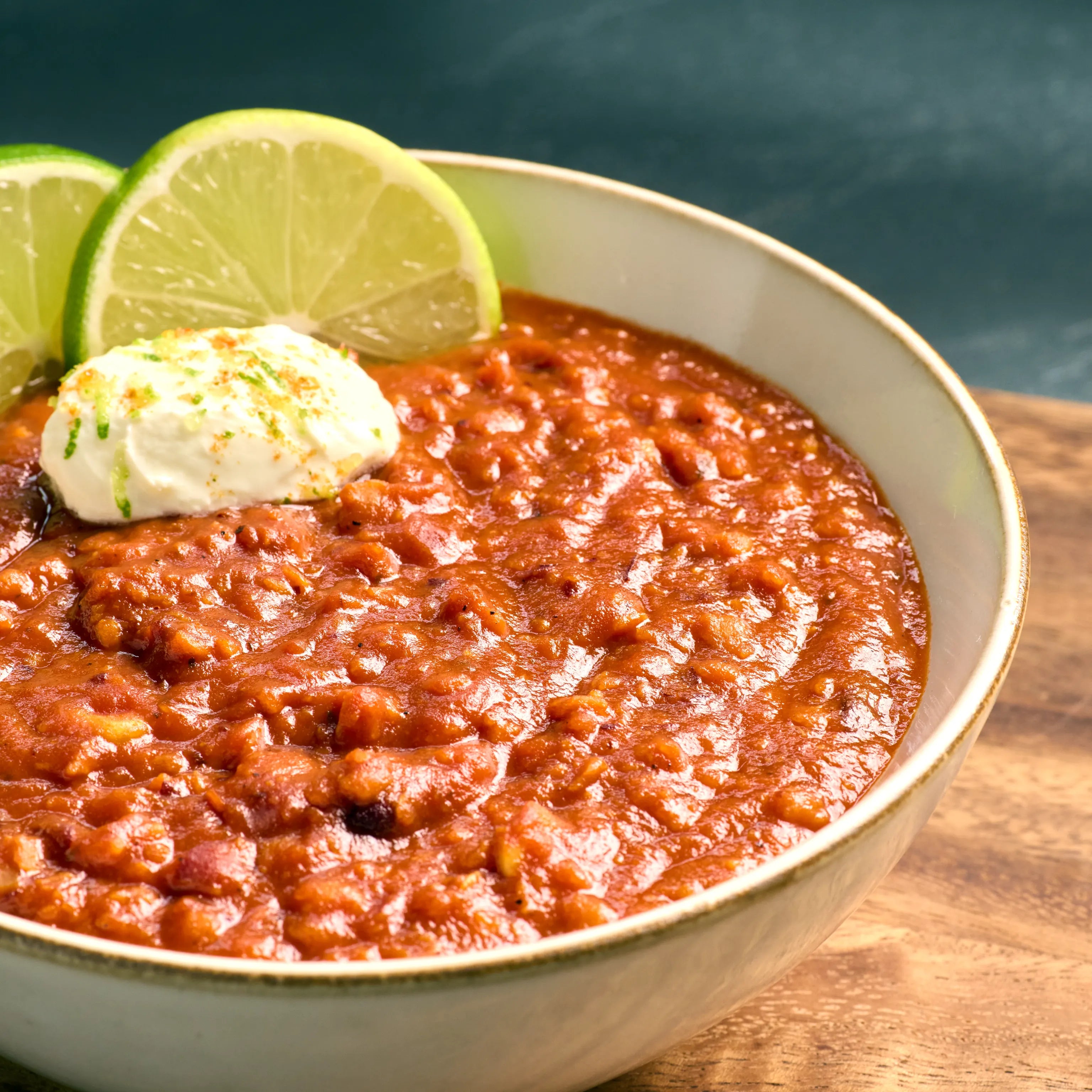 Schüssel mit rotem Chili oder Eintopf, garniert mit einem Klecks Sauerrahm und zwei Limettenscheiben am Rand