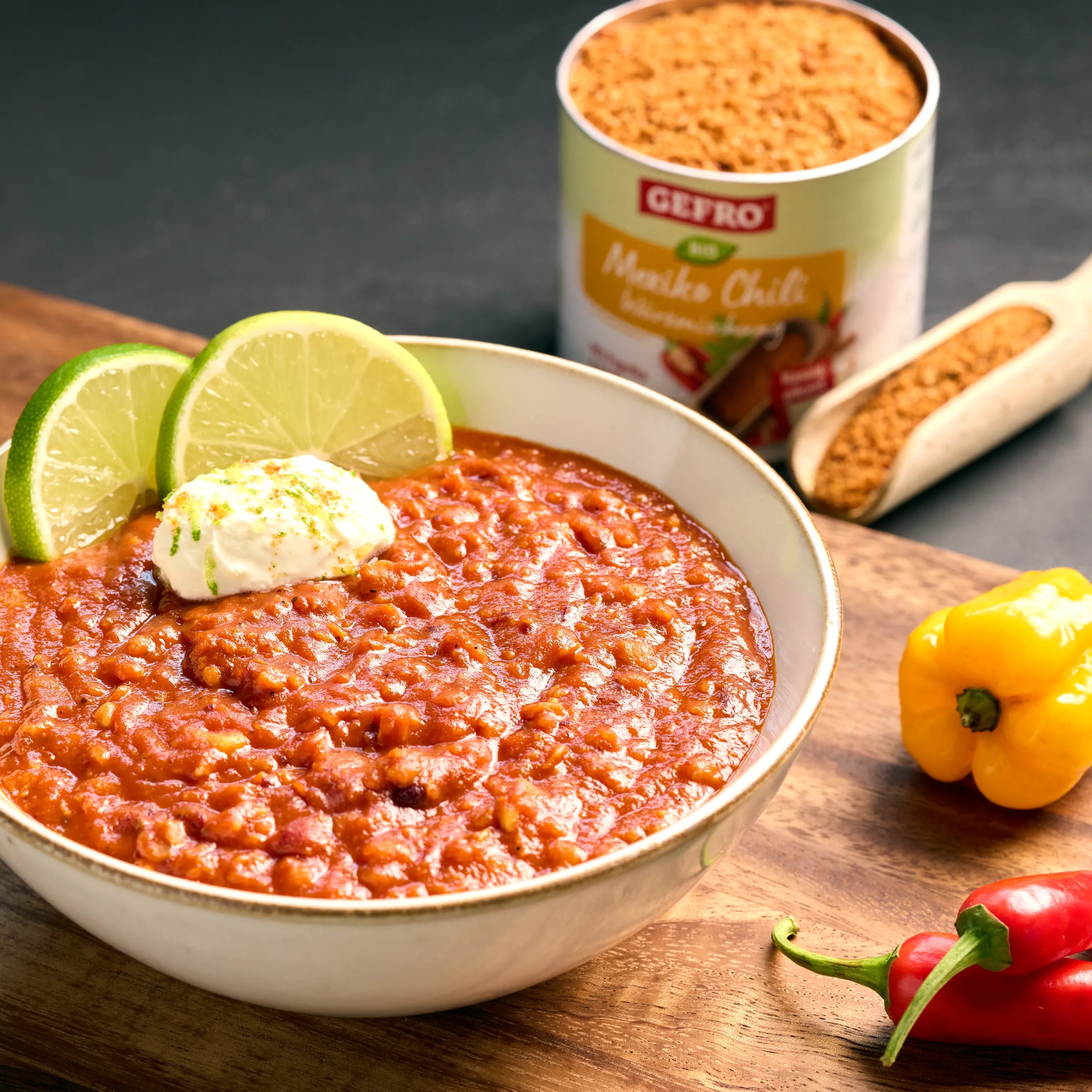 Schüssel mit rotem Chili sin Carne, garniert mit Limettenscheiben und einem Klecks Creme, daneben Gewürz und Paprika