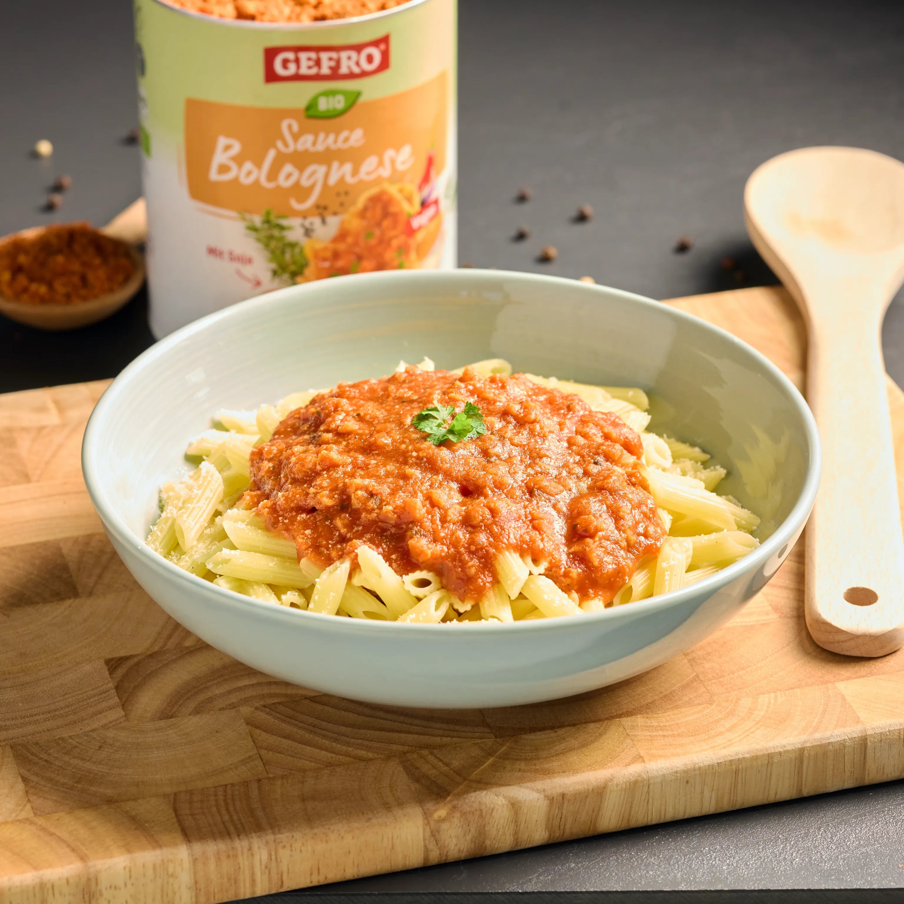 Schüssel mit Penne und Bolognese-Soße auf Holzbrett, dahinter Dose von Gefro Bio Sauce Bolognese.
