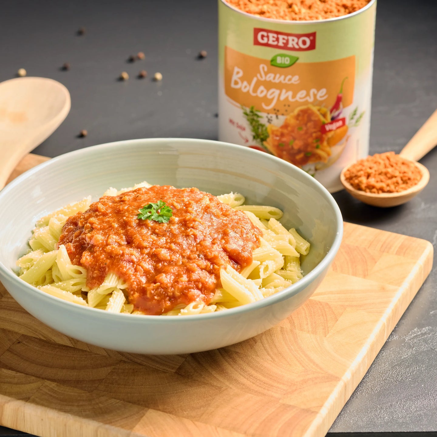 Schüssel mit Penne und Bolognese-Sauce auf Holzbrett, daneben Dose Gefro Bio Sauce Bolognese und Holzlöffel