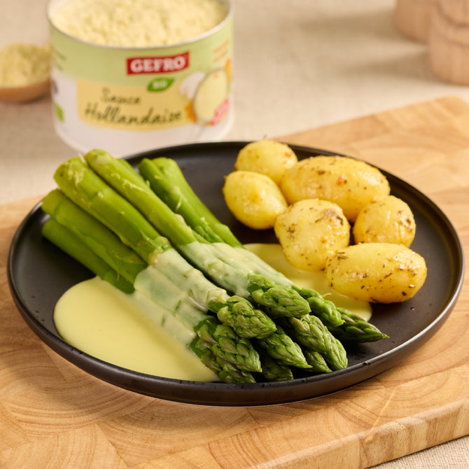 Grüner Spargel mit Sauce Hollandaise und kleinen Kartoffeln auf schwarzem Teller, passend als Serviervorschlag.