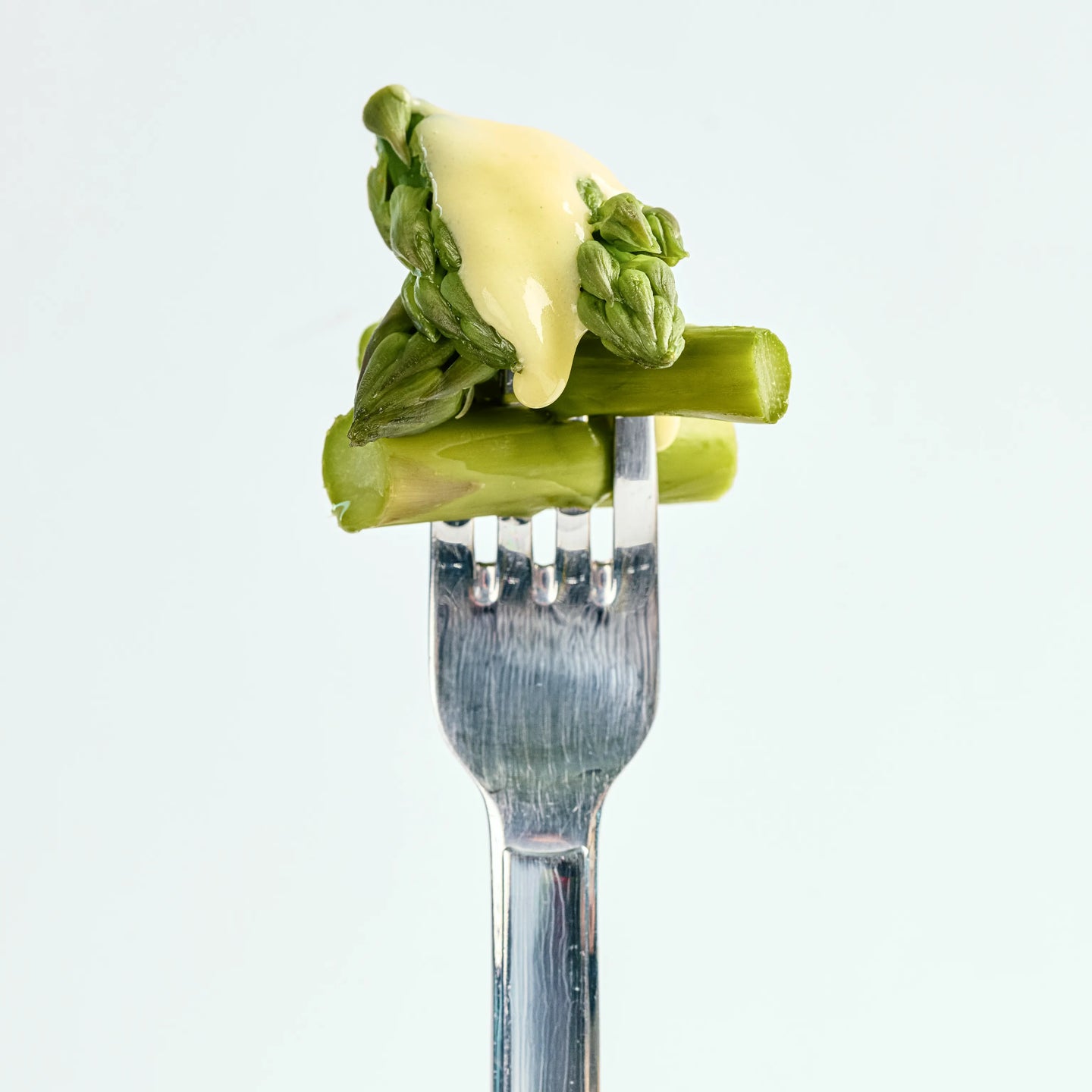 Grüne Spargelstücke auf einer Gabel mit heller Sauce, nah aufgenommen vor schlichtem, hellem Hintergrund