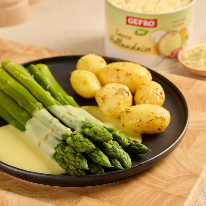 Grüner Spargel mit heller Sauce und kleinen Kartoffeln auf schwarzem Teller, dazu Produktdose im Hintergrund
