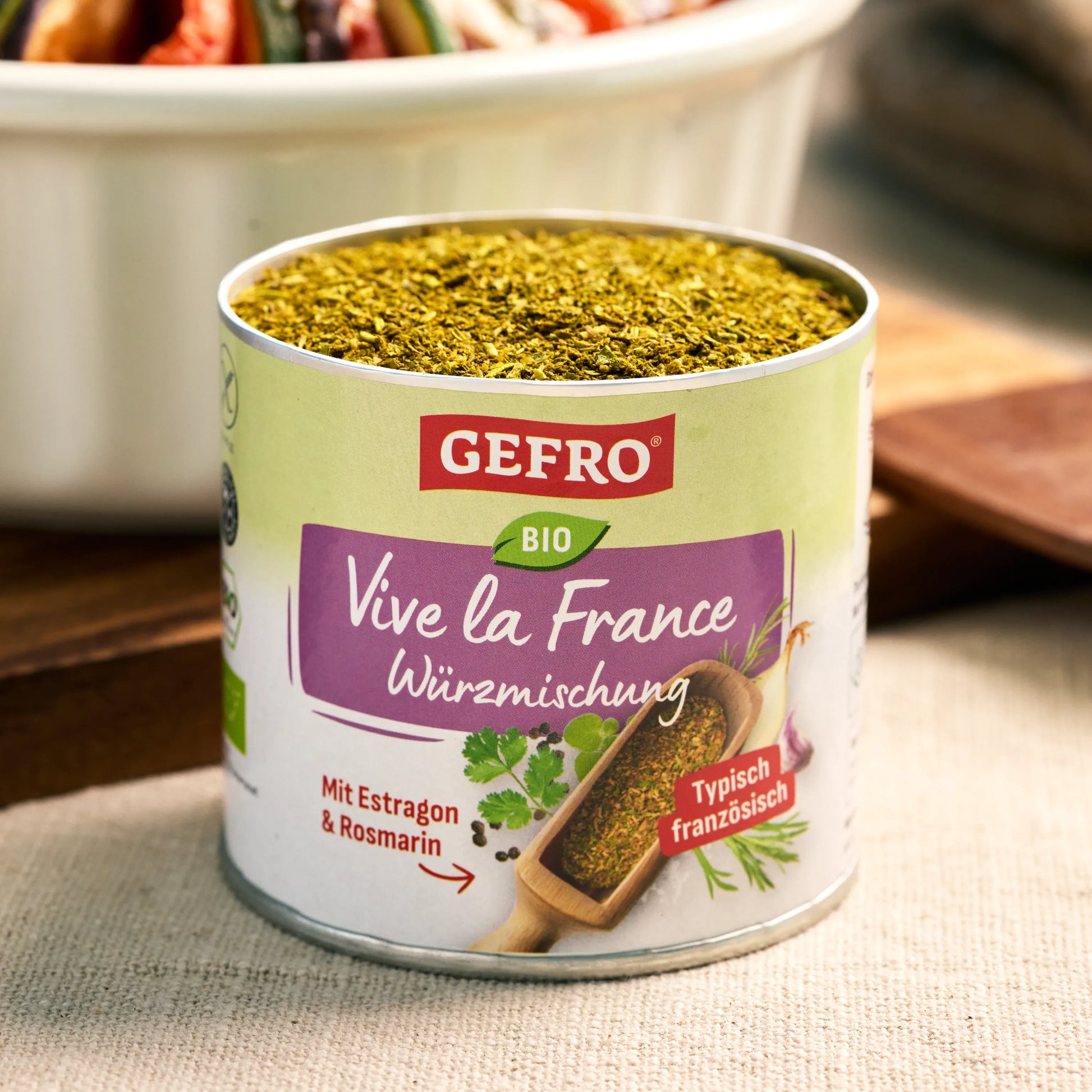 Dose mit GEFRO Bio Würzmischung Vive la France, geöffnet und gefüllt mit grüner Kräutermischung auf Tisch.