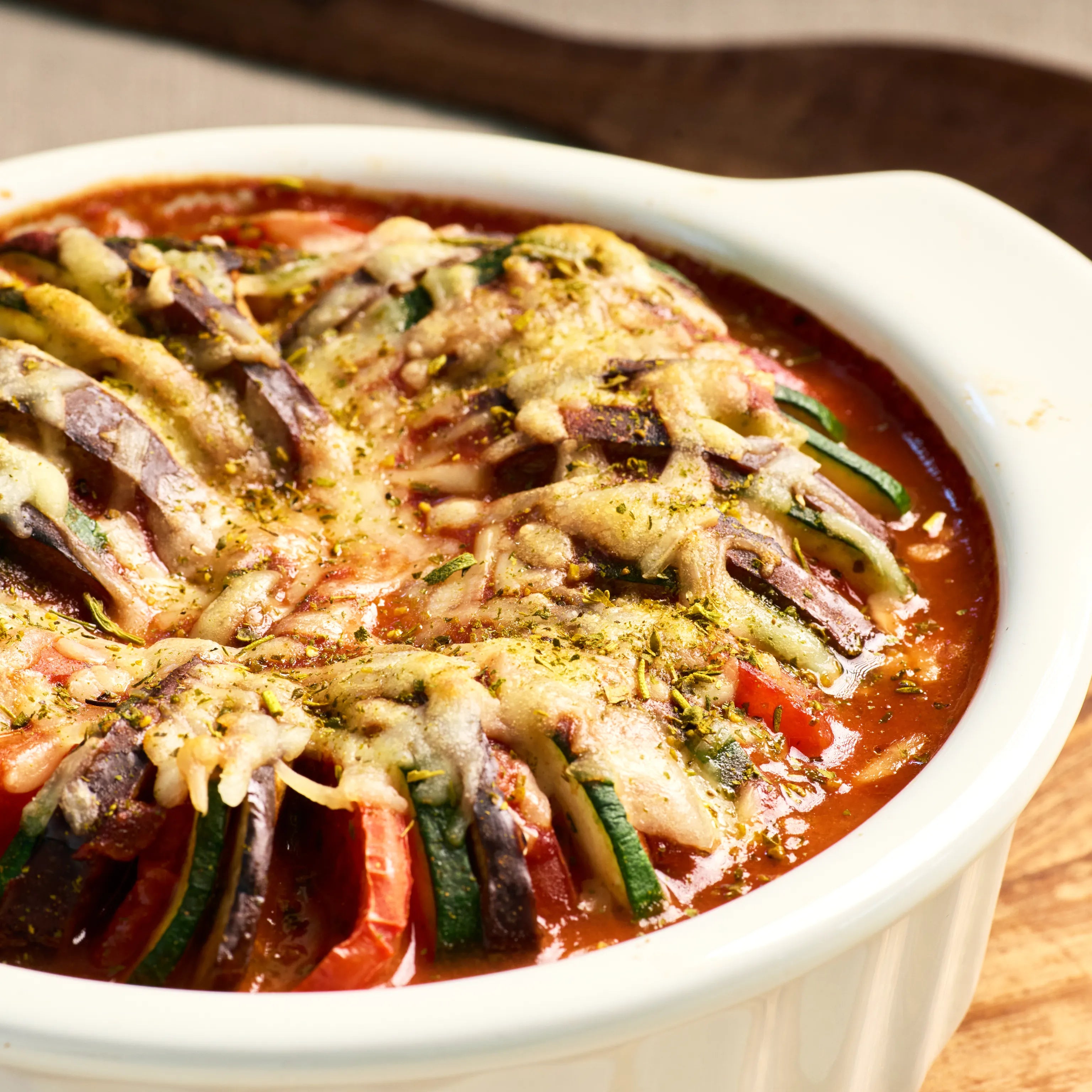 Auflauf mit Tomatensoße, Zucchini, Aubergine und Käse in weißer Form, frisch gebacken und servierfertig