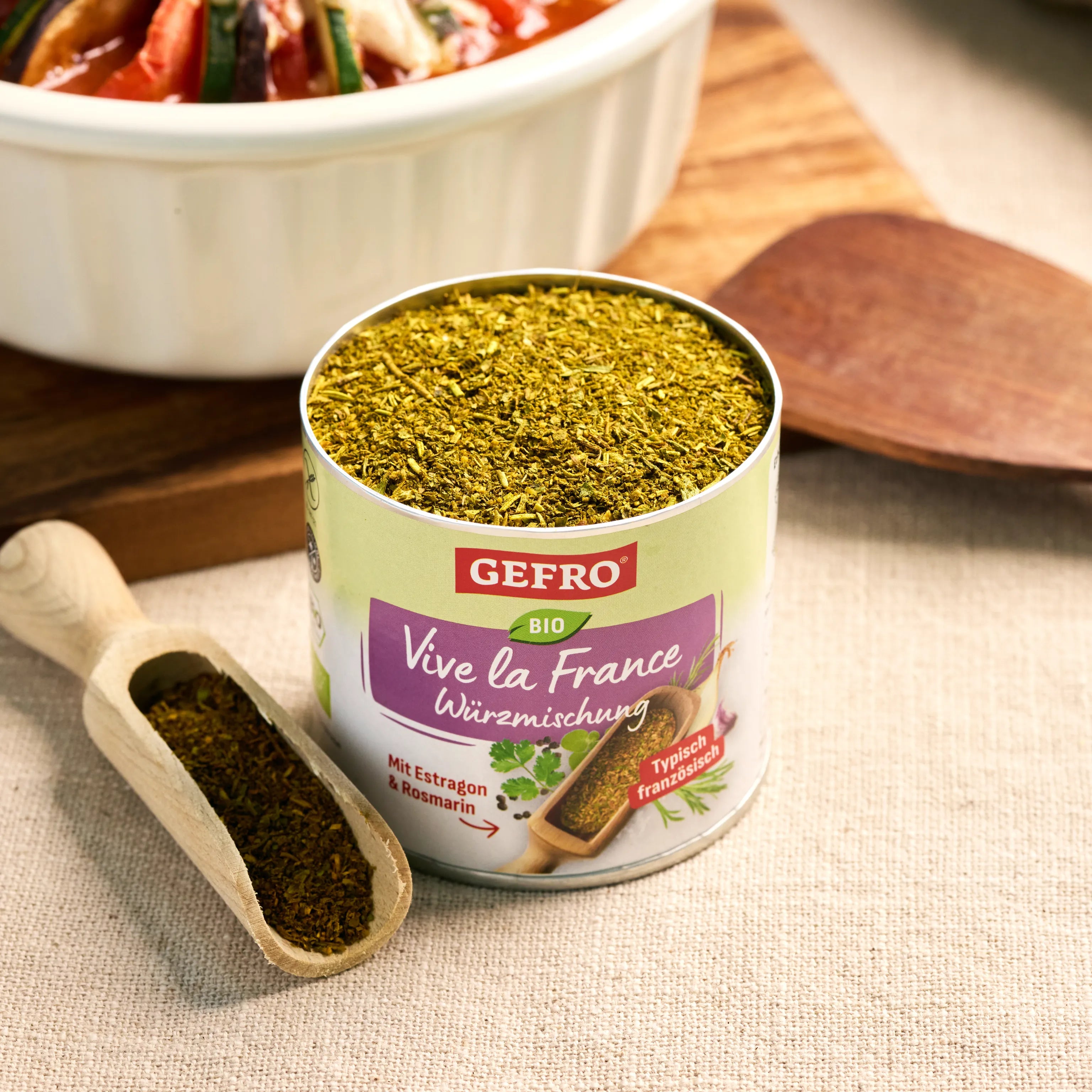 Offene Dose GEFRO Bio Vive la France Würzmischung mit Kräutern, daneben Holzschaufel auf hellem Tuch in Küche