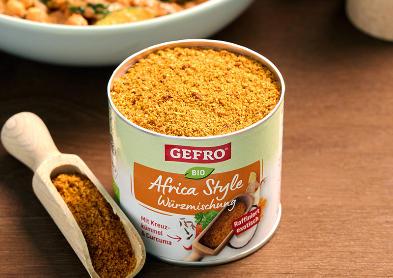 Dose GEFRO Bio Africa Style Würzmischung auf Holztisch, daneben Holzschaufel mit Gewürzpulver in Nahaufnahme