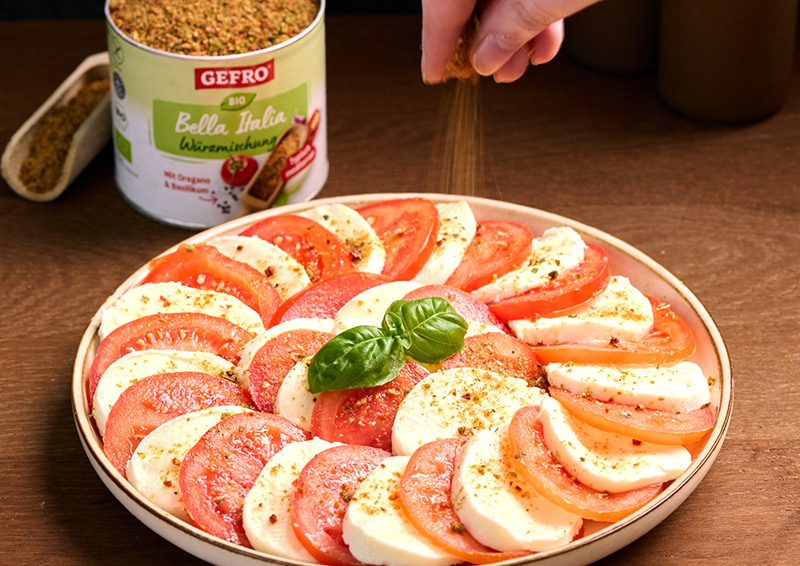 Caprese-Salat mit Tomaten, Mozzarella und Basilikum auf Teller, während Bella Italia Würzmischung darüber gestreut wird