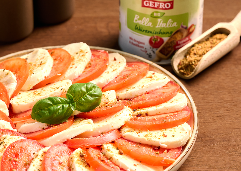 Caprese-Salat auf Teller mit Tomaten, Mozzarella und Basilikum, daneben Gewürzmischung und geöffnete Schaufel##