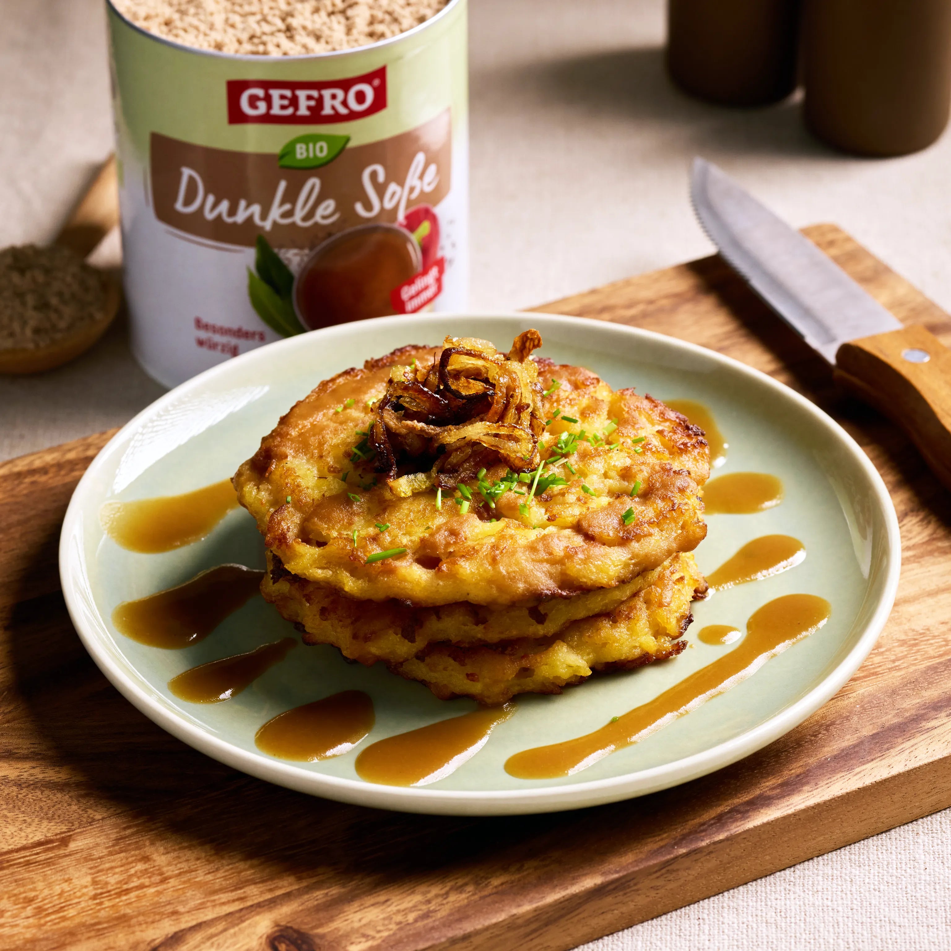 Zwei goldbraune Kartoffelpuffer auf einem Teller mit dunkler Soße und Röstzwiebeln, daneben GEFRO Bio Dunkle Soße.