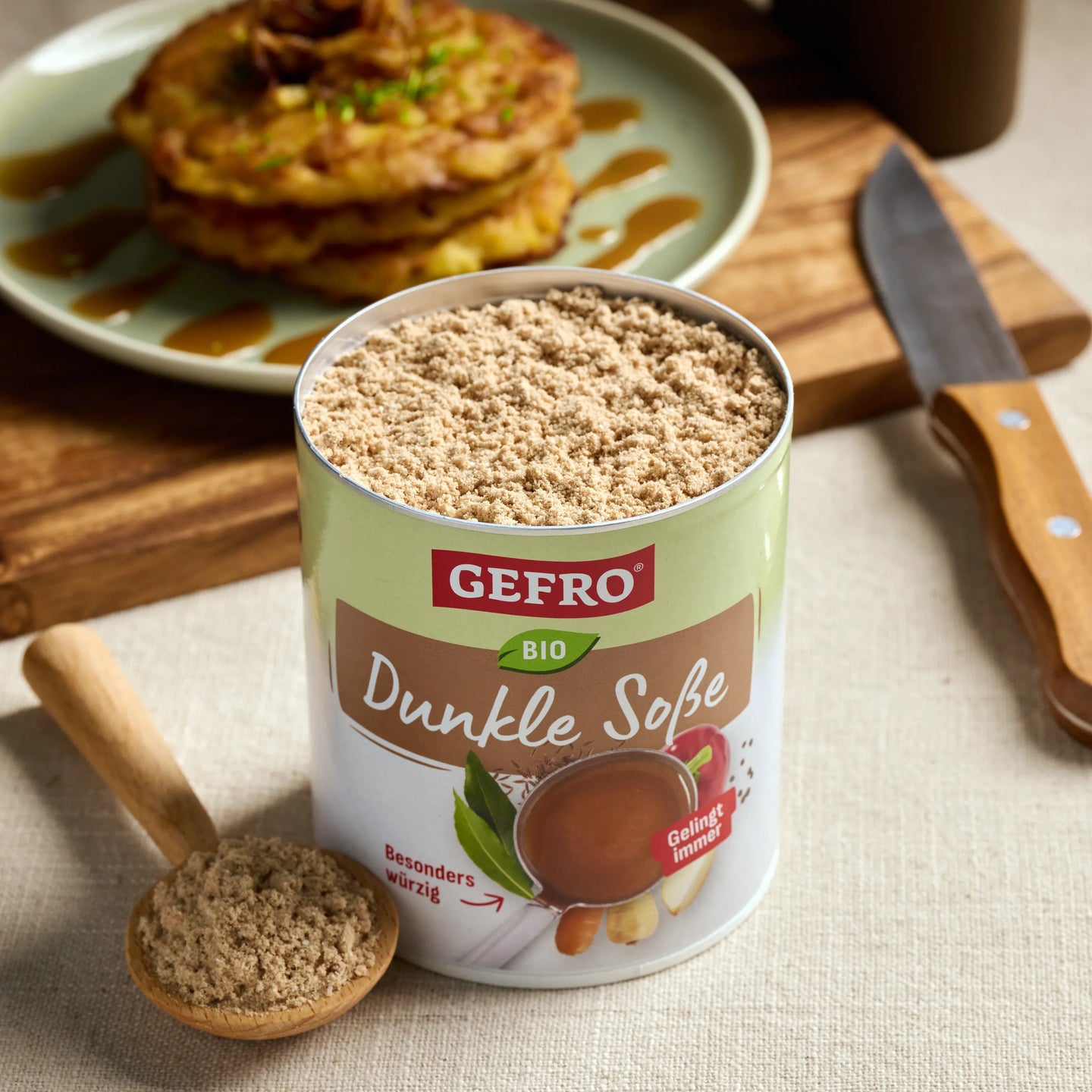 Offene Dose GEFRO Bio Dunkle Soße mit Pulver und Holzlöffel auf Tisch, dahinter ein Teller mit Gericht