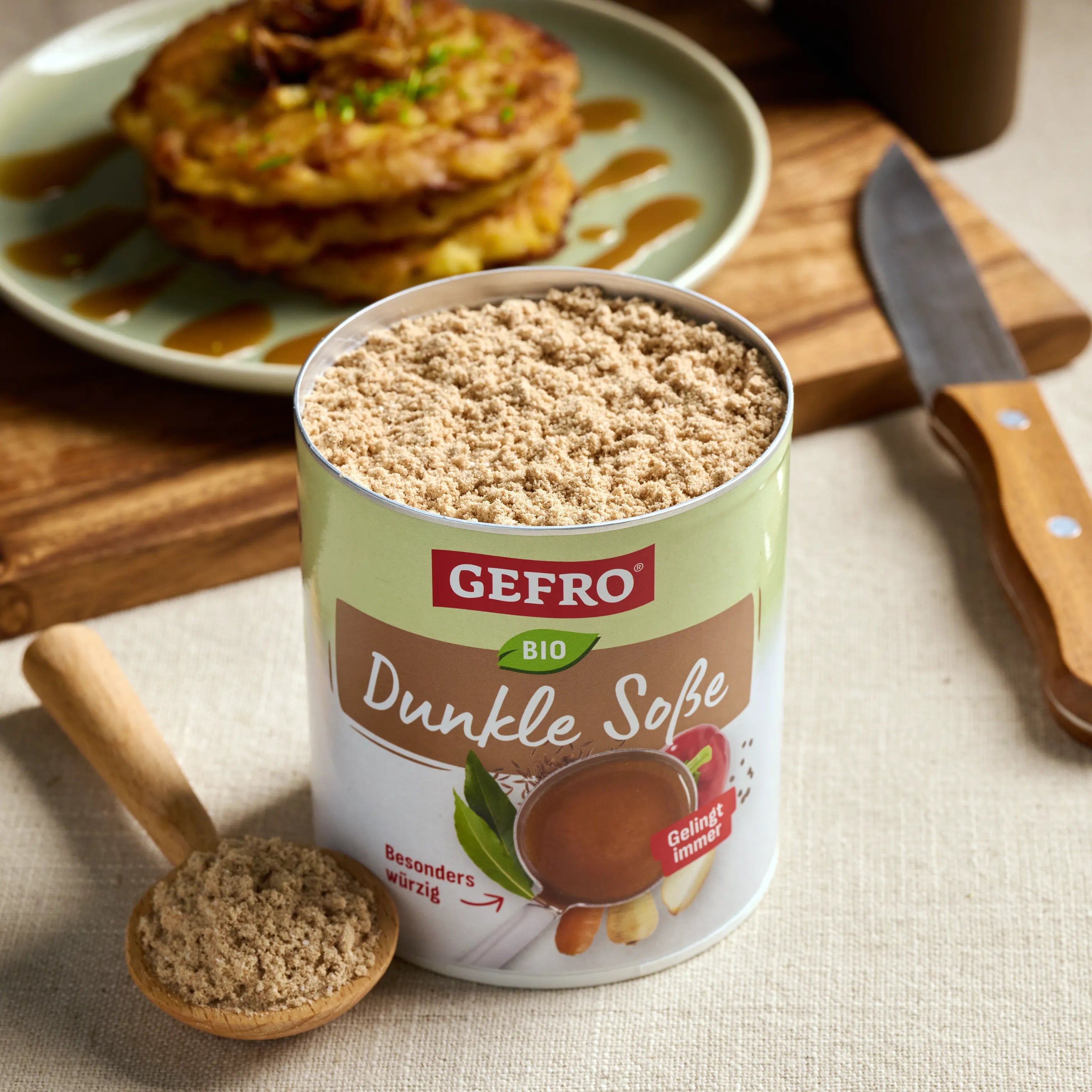 Offene Dose GEFRO Bio Dunkle Soße mit Pulver und Holzlöffel auf Tisch, dahinter ein Teller mit Gericht