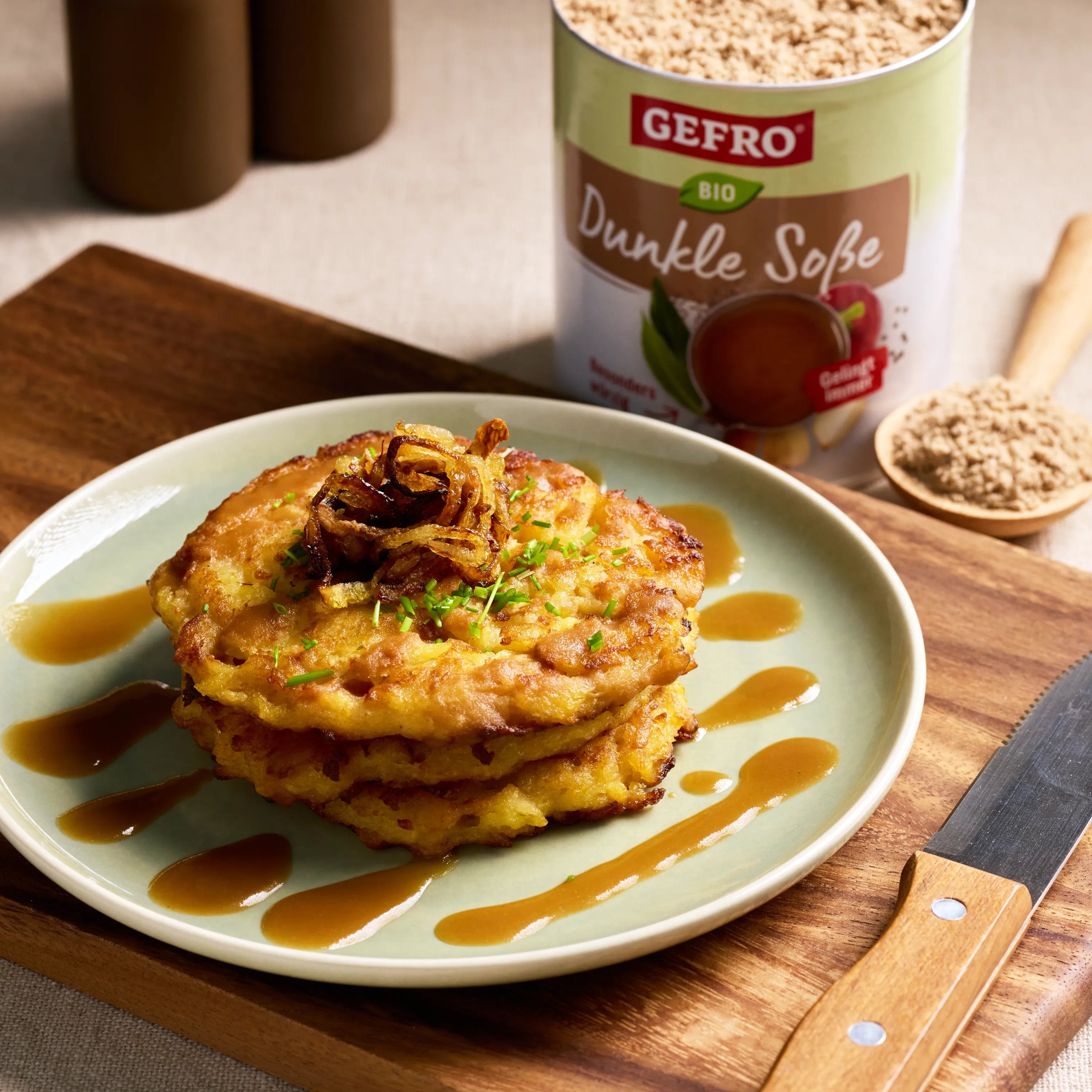 Kartoffelpuffer mit dunkler Soße und Röstzwiebeln auf einem Teller, daneben GEFRO Bio Dunkle Soße im Hintergrund