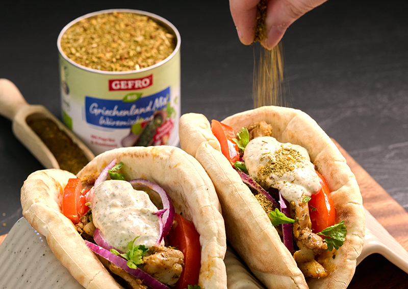Zwei gefüllte Pita-Taschen mit Fleisch, Tomaten, roten Zwiebeln und Kräutersoße, darüber wird Gewürz gestreut.