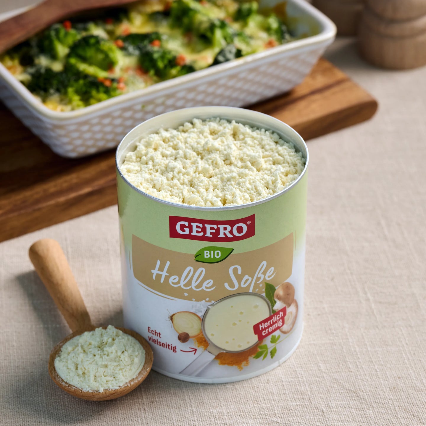 Dose GEFRO Bio Helle Soße mit cremigem Soßenpulver und Holzlöffel, davor ein Gemüseauflauf im Hintergrund