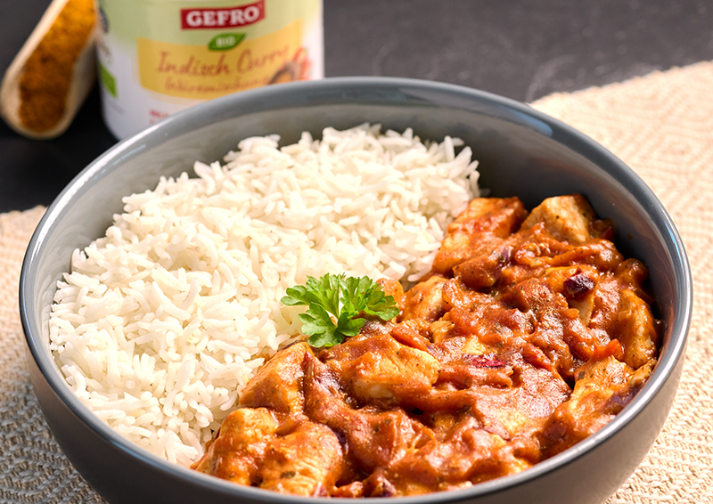 Schüssel mit weißem Reis und cremigem Hähnchen-Curry, garniert mit Petersilie, als servierfertige Mahlzeit