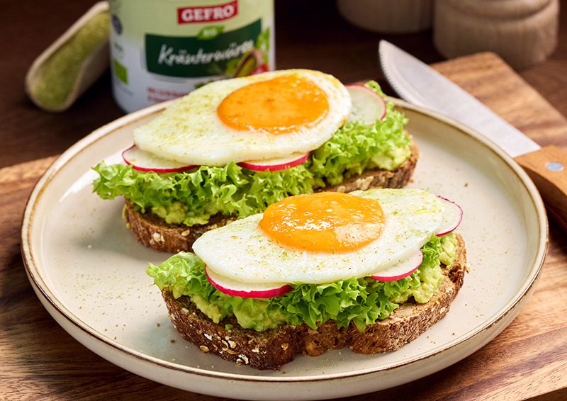 Zwei Brote mit Avocado, Salat, Radieschen und Spiegelei auf einem Teller, serviert auf einem Holzbrett