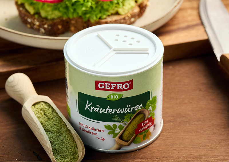 Dose GEFRÖ Bio Kräuterwürze auf Holztisch neben Holzschaufel mit Gewürz, passend zum Würzen von Speisen