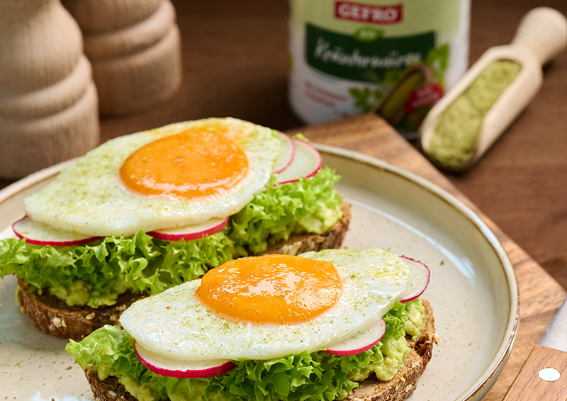Zwei belegte Brote mit Salat, Radieschen und Spiegelei auf einem Teller, serviert als frische Mahlzeit.