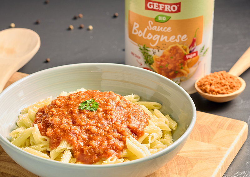 Schüssel mit Penne und Bolognese-Sauce, daneben Gefro Bio Sauce Bolognese und ein Löffel mit Pulver