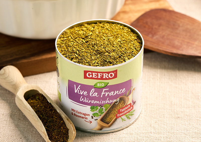 Offene Dose GEFRO Bio Würzmischung Vive la France, gefüllt mit Kräutern, daneben eine kleine Holzschaufel.