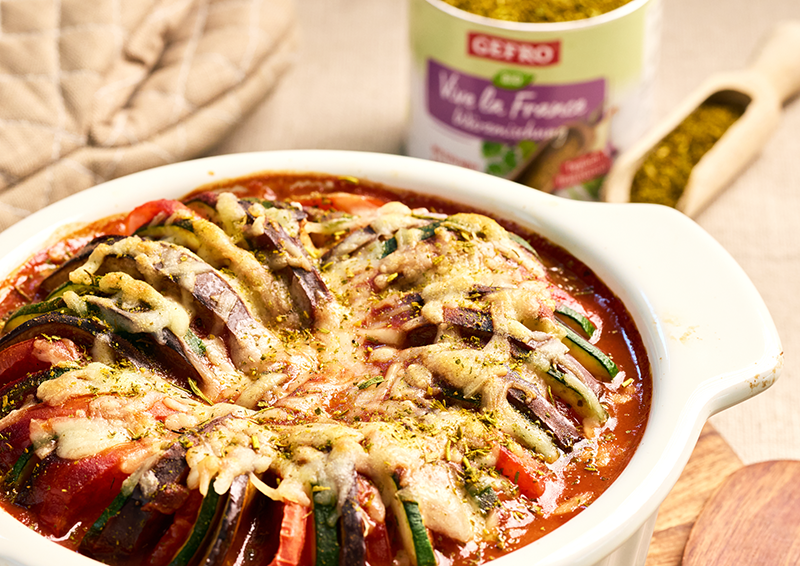 Überbackenes Ratatouille in weißer Auflaufform mit Tomaten, Zucchini und Auberginen in würziger Sauce.
