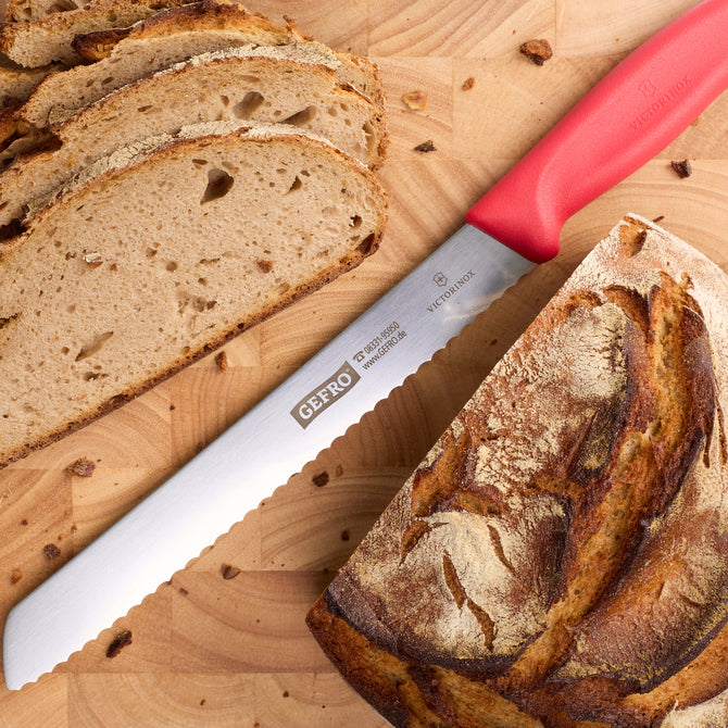 Brotmesser mit rotem Griff auf Holzbrett neben angeschnittenem Laib und Brotscheiben zum sauberen Schneiden